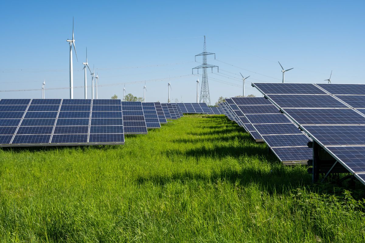 photo of solar panels in a grassy field with transmission lines and wind turbines in the background symbolizing the possibility of independent community solar, how it could help Hoosiers and that it could be part of a broader energy mix